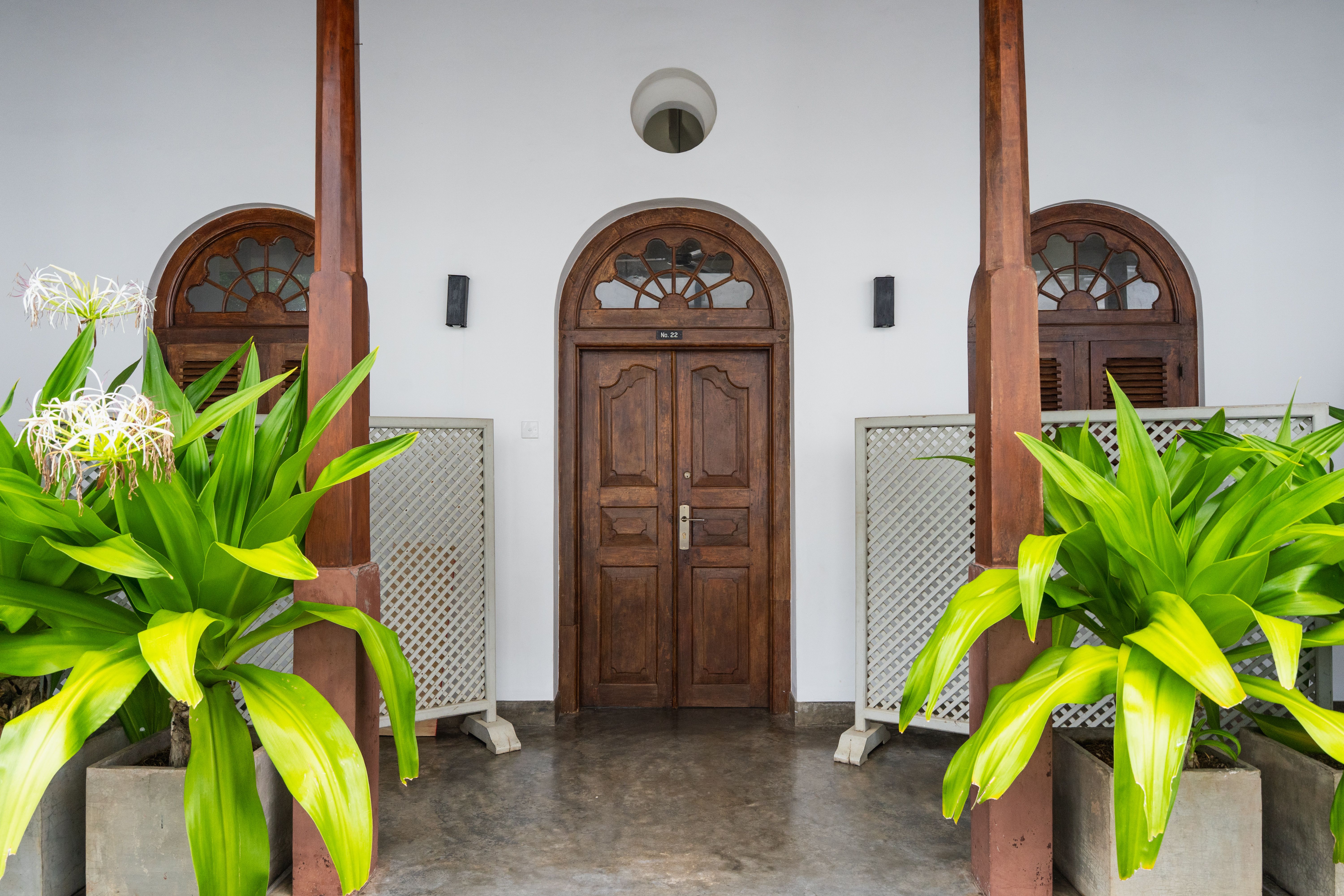 Charming entrance with wooden door flanked by lush tropical greenery, creating a welcoming atmosphere.