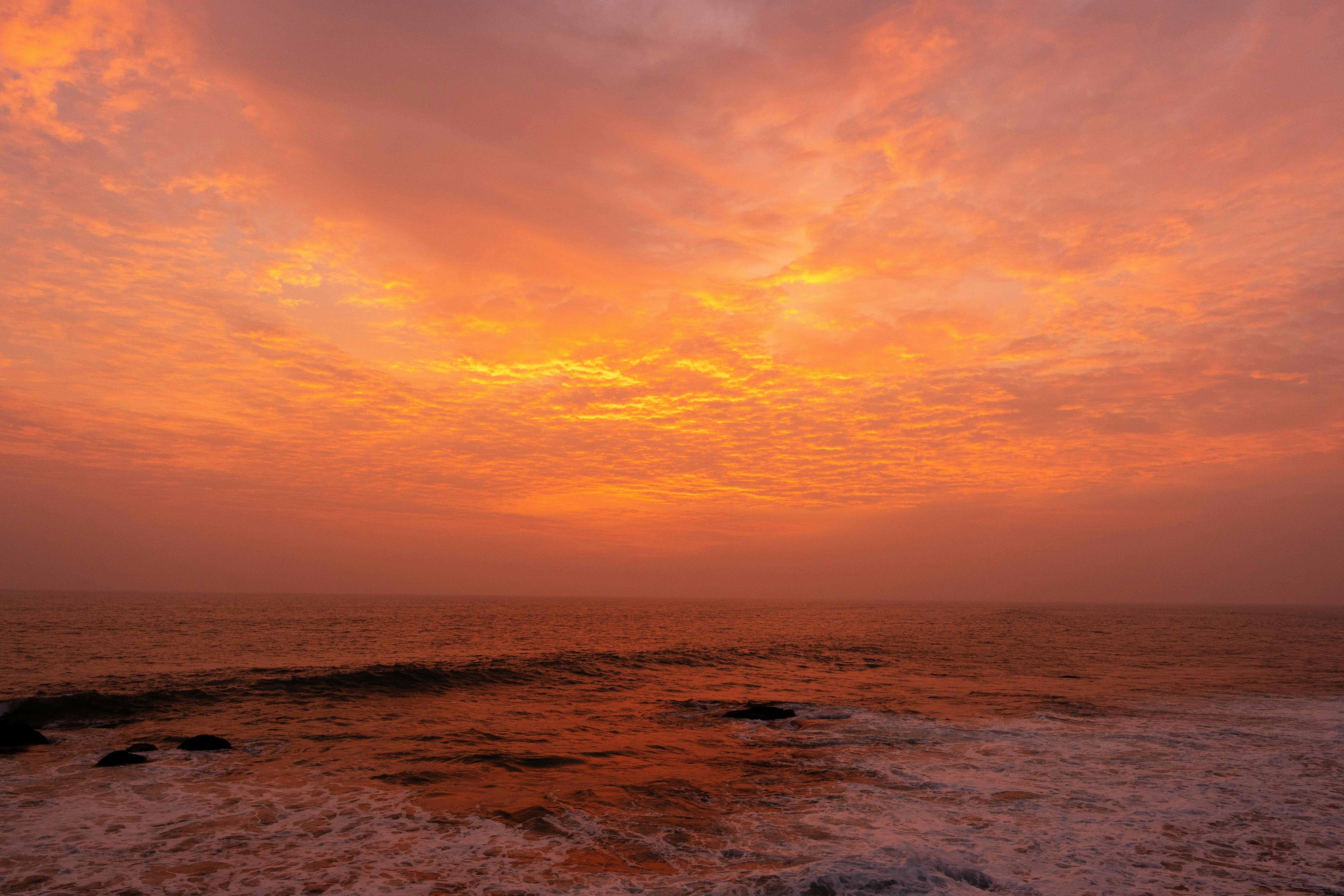 Stunning sunset casting orange hues over a tranquil ocean with gentle waves.