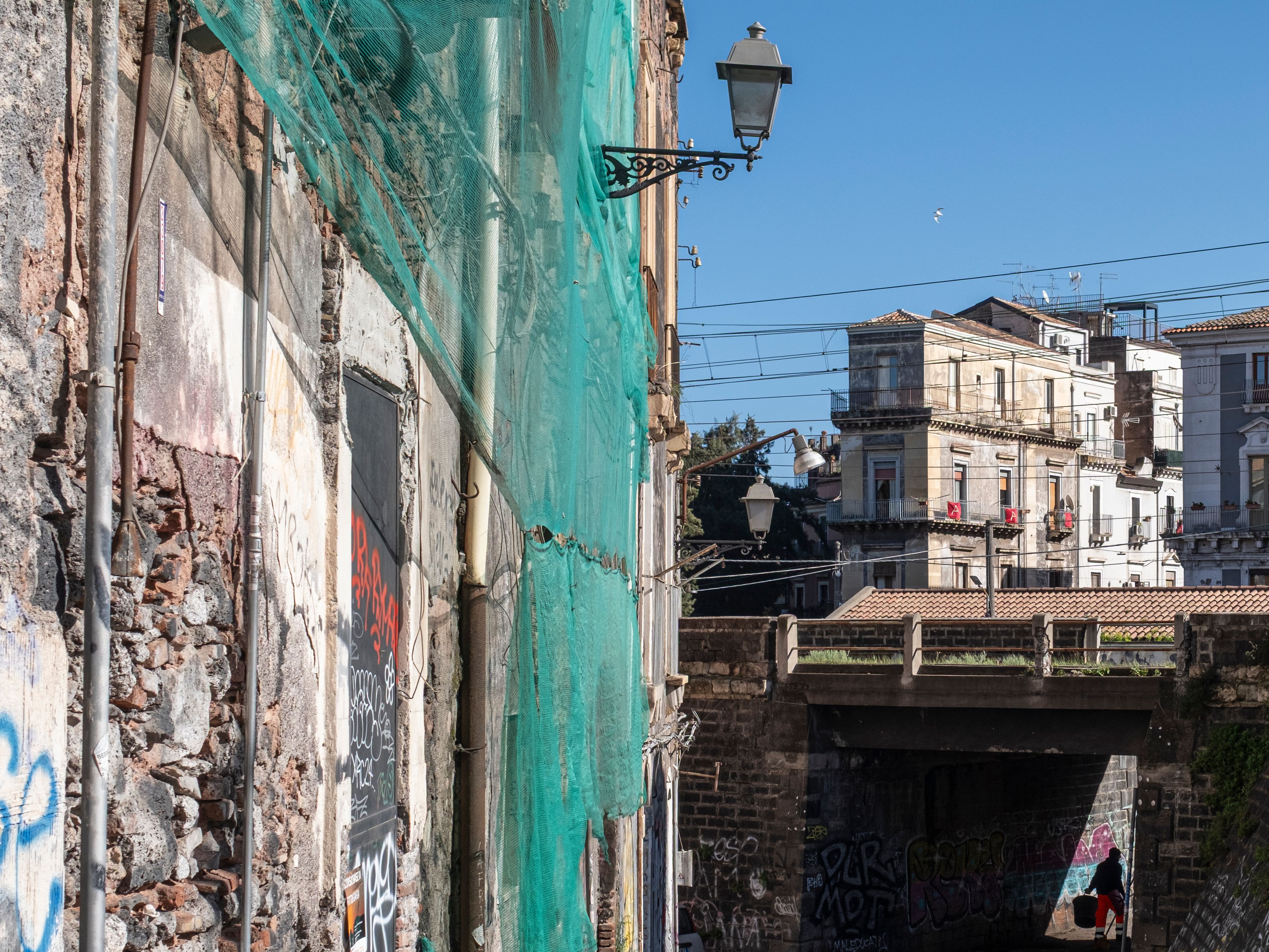 Urban view of Catania, Sicily, featuring graffiti, historic architecture, and a bright day.