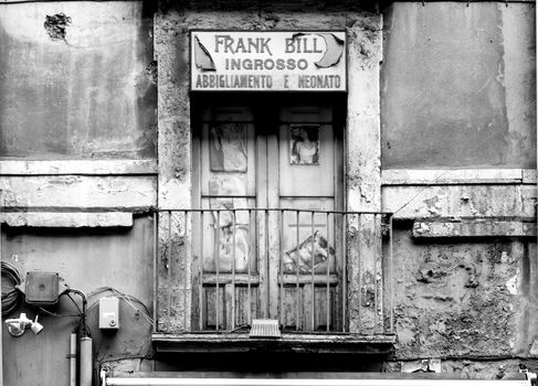 Black and white image of an old storefront in Catania, Sicily, with a weathered facade and vintage charm.