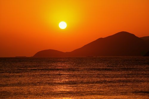 Free Captivating sunset over calm sea with silhouette hills under vibrant orange sky. Stock Photo