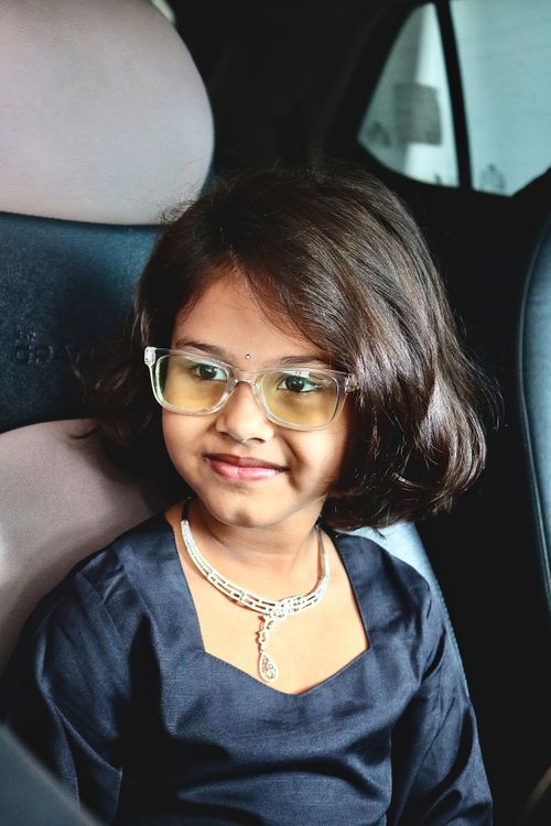 Free Portrait of a smiling child with glasses sitting in a car seat wearing a necklace. Stock Photo