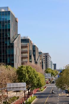 A bustling city street lined with contemporary glass buildings under a clear blue sky.