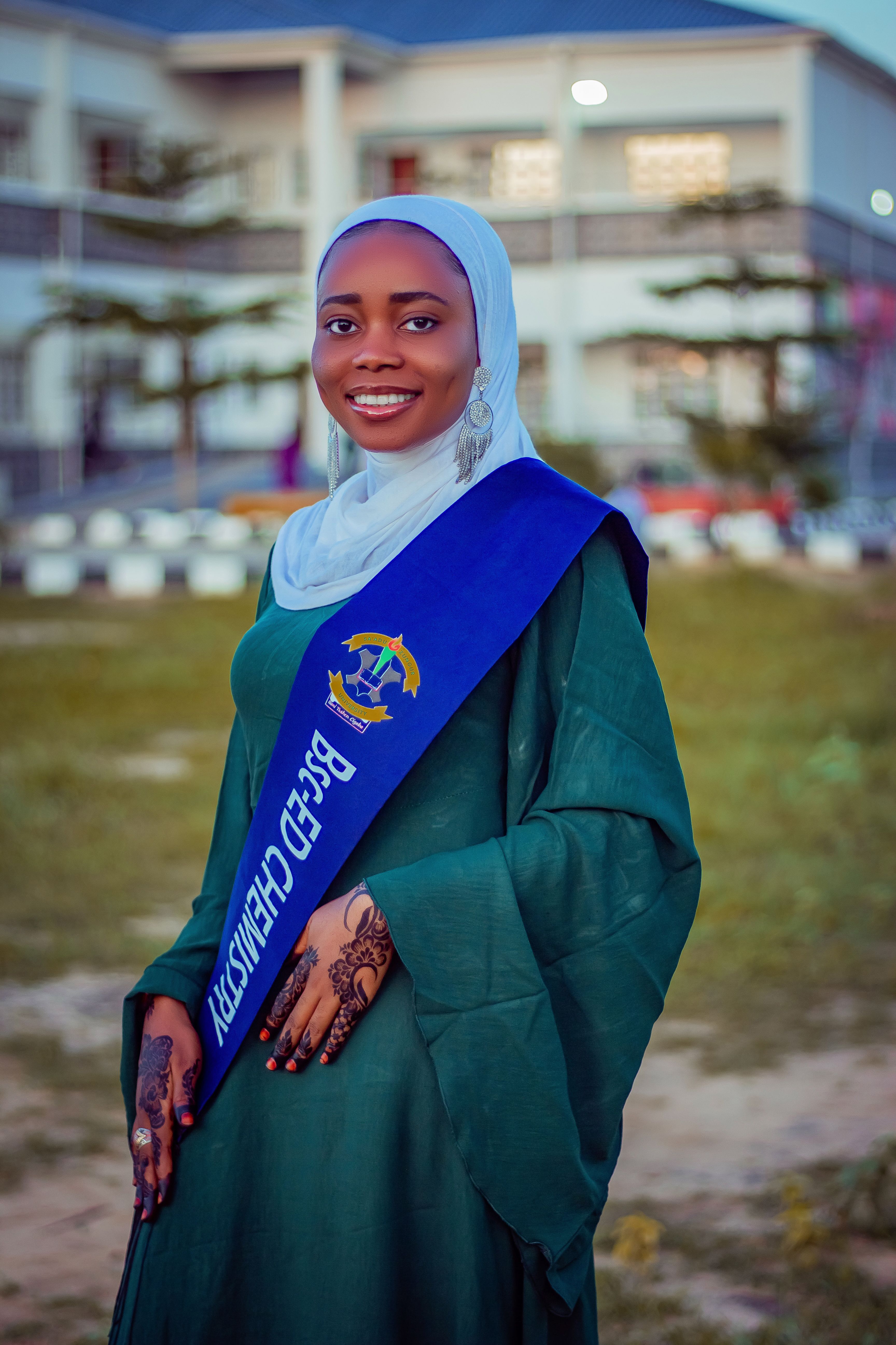 A smiling young woman in hijab during her chemistry graduation ceremony outdoors.