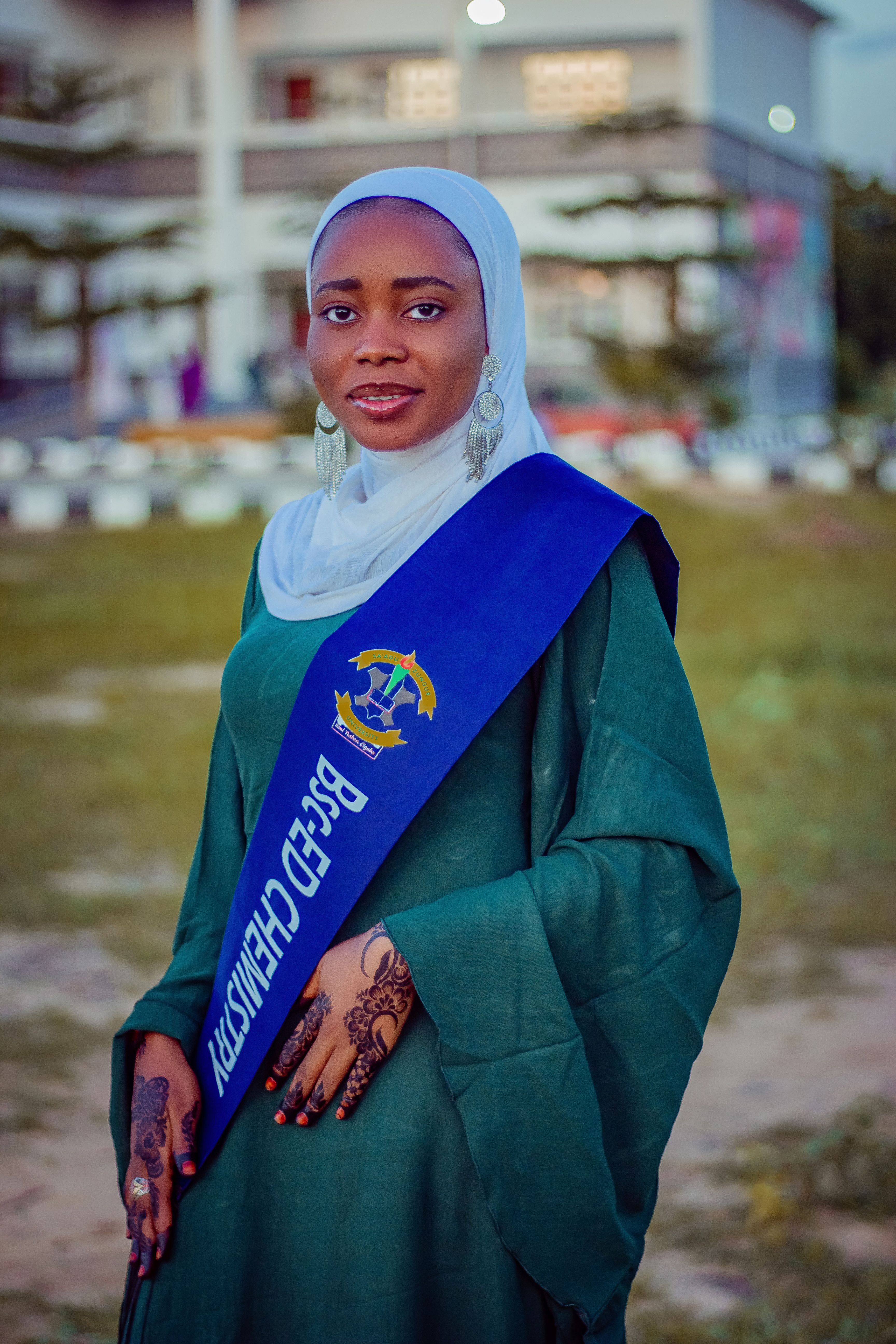 Young woman in hijab with chemistry sash at outdoor graduation ceremony.