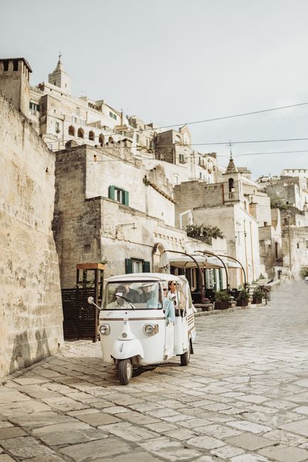 Classic white tuk-tuk driving through a historic Italian alley in warm daylight.