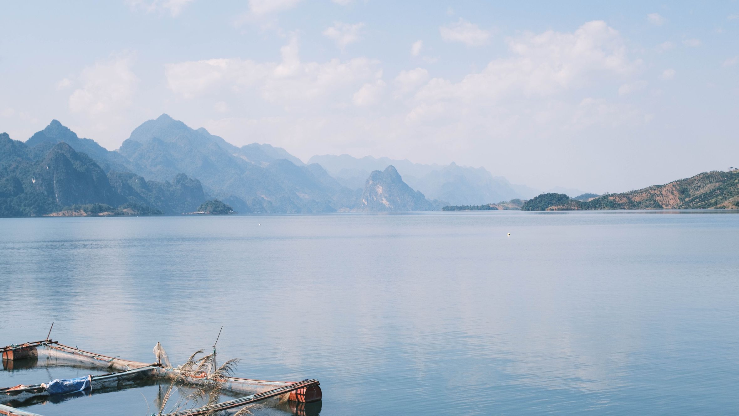 A serene mountain lake with clear blue sky and distant peaks reflecting in the calm water.