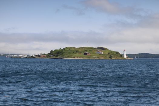 Scenic view of an island with a lighthouse surrounded by blue sea under a partly cloudy sky.