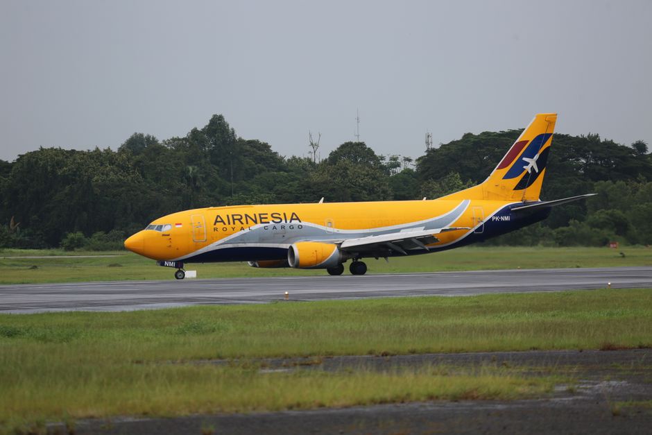 Airnesis cargo airplane taxiing on the runway of Jakarta airport with lush greenery in the background.