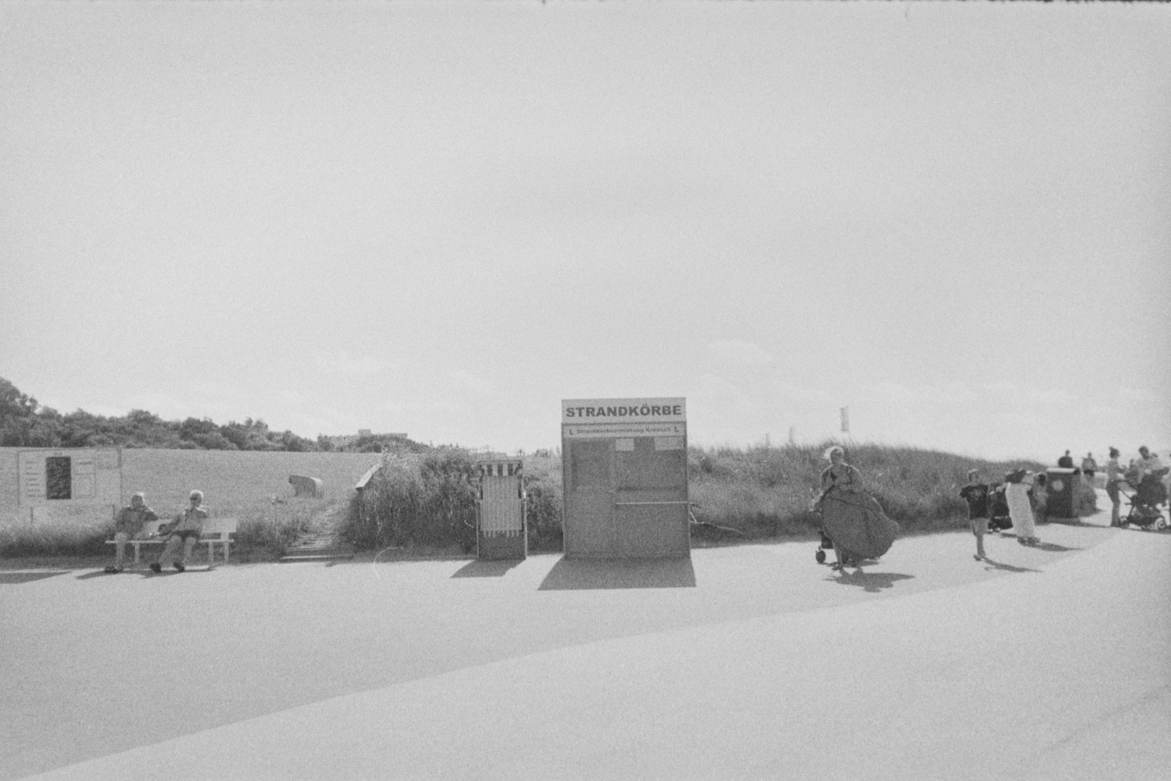 無料 Strandkörbe のレンタル ブースと歩いている人々がいるビーチ エリアの白黒写真。 写真素材