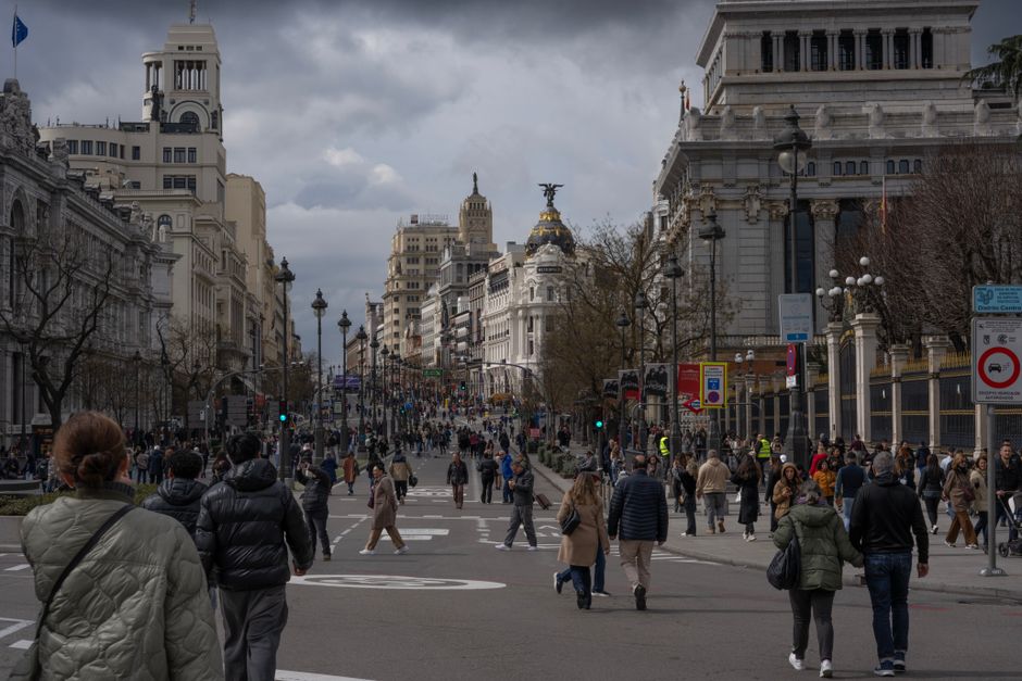Concurrida escena callejera en el centro de la ciudad de Madrid con arquitectura icónica y peatones bulliciosos bajo un cielo nublado.
