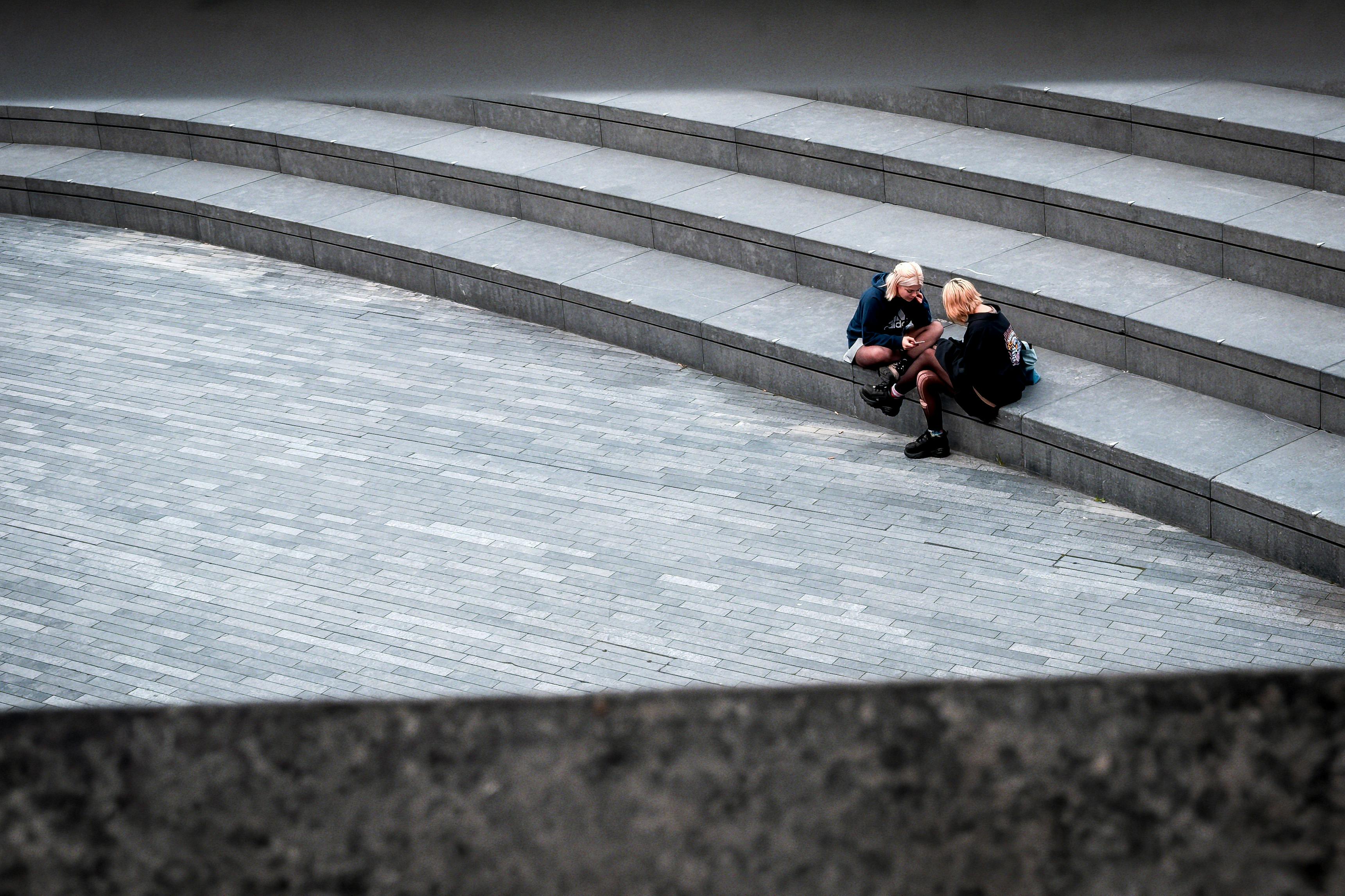 Gratuit Deux jeunes adultes discutent sur des marches en pierre d'un immeuble à l'architecture moderne. Photos