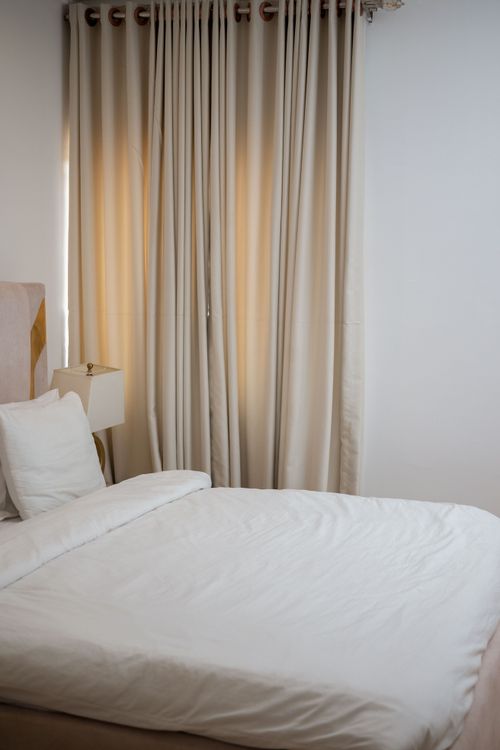 Free A calm and inviting bedroom featuring a neatly made bed, curtains, and a soft ambiance. Stock Photo