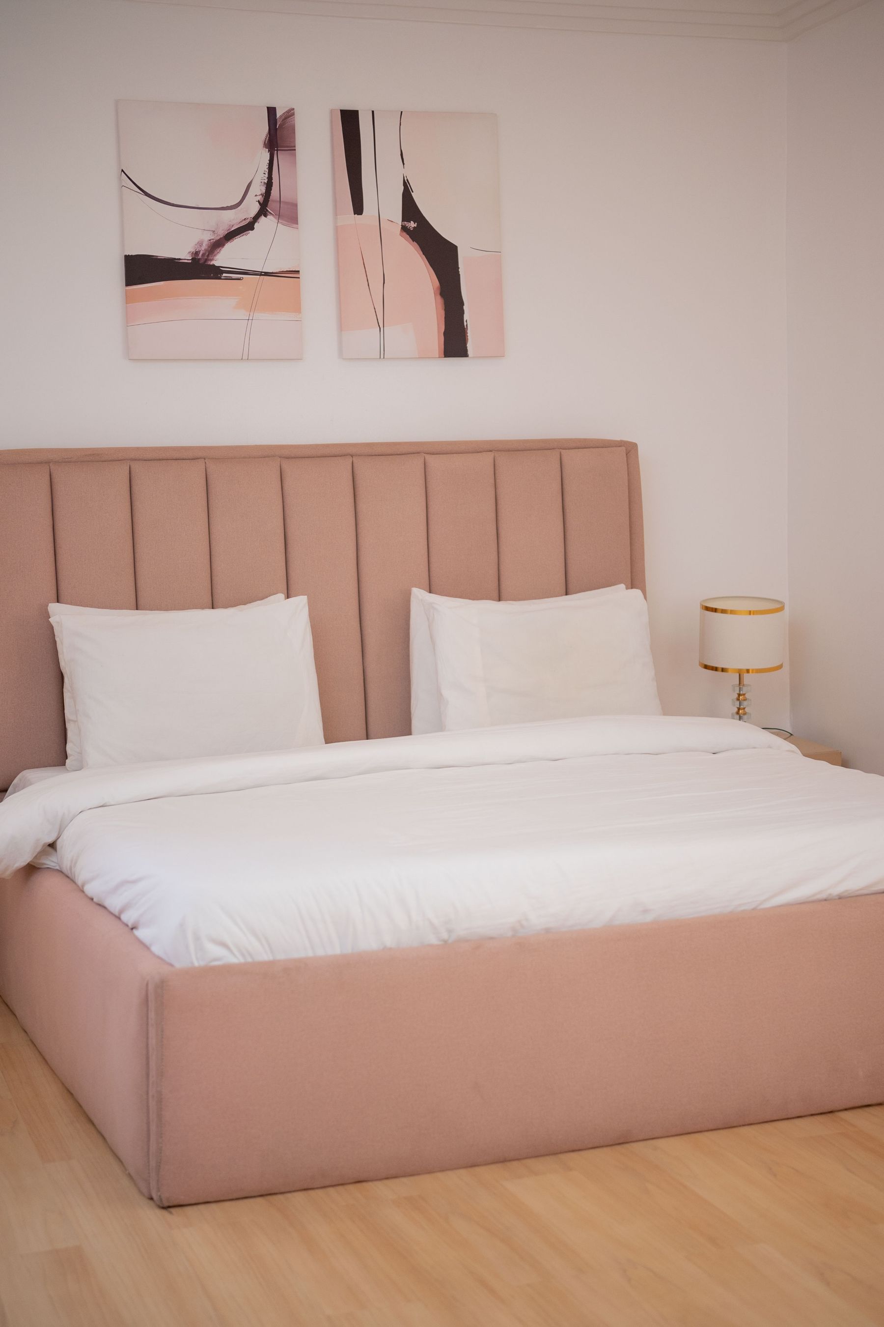 Serene bedroom with a blush upholstered bed, pale timber floor and white bedding