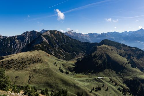 Free A breathtaking view of lush green hills set against majestic alpine mountains under a clear blue sky. Stock Photo