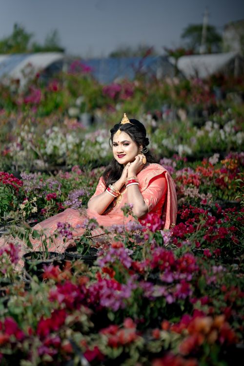 Free A woman in traditional attire poses gracefully surrounded by colorful flowers outdoors. Stock Photo