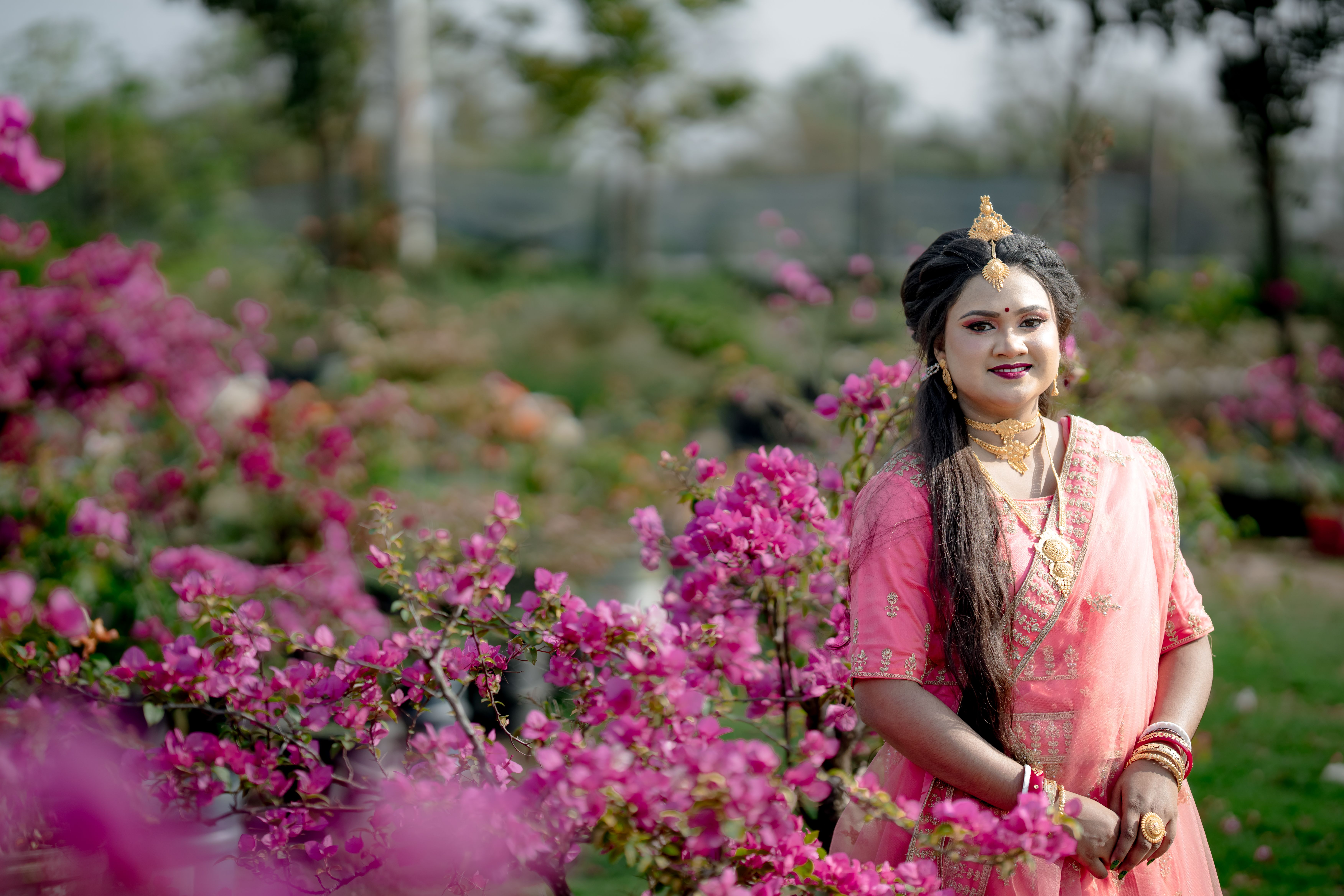 A joyful woman in pink attire enjoys a sunny day in a garden full of bright bougainvillea flowers.