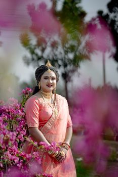A woman in traditional attire poses amidst vibrant flowers, exuding elegance and joy in an outdoor setting.