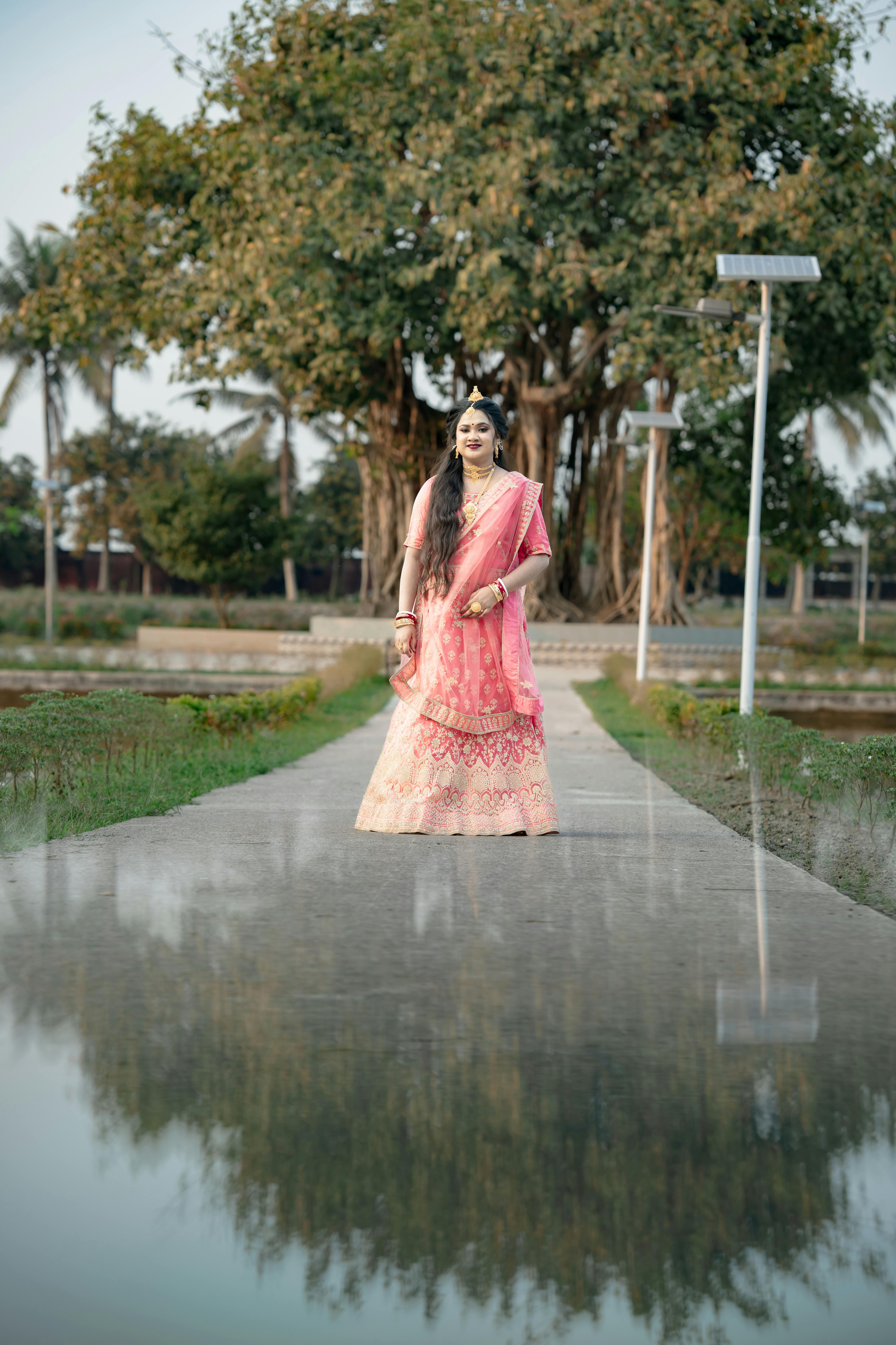 Gratis Una donna in abito tradizionale rosa cammina lungo un sentiero con uno sfondo panoramico. Foto a disposizione