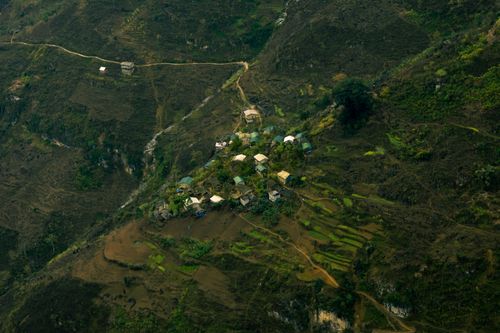 Free Scenic aerial view of a remote mountain village surrounded by lush greenery and terraced fields. Stock Photo