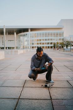 A man crouches while controlling a drone outside a modern architectural structure.