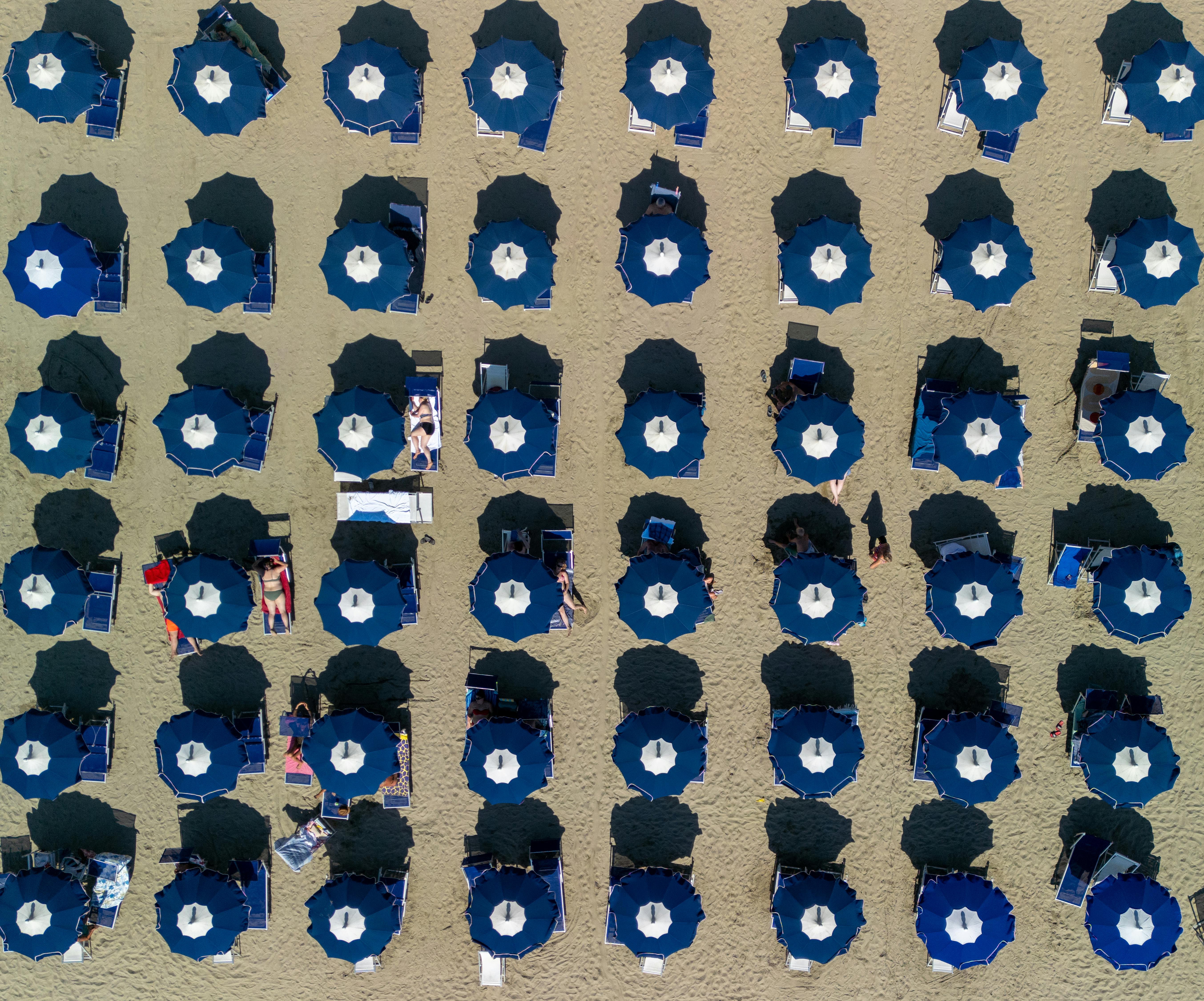 Kostnadsfria Flygbild av blå parasoller arrangerade i rader på en italiensk sandstrand. Stock foto