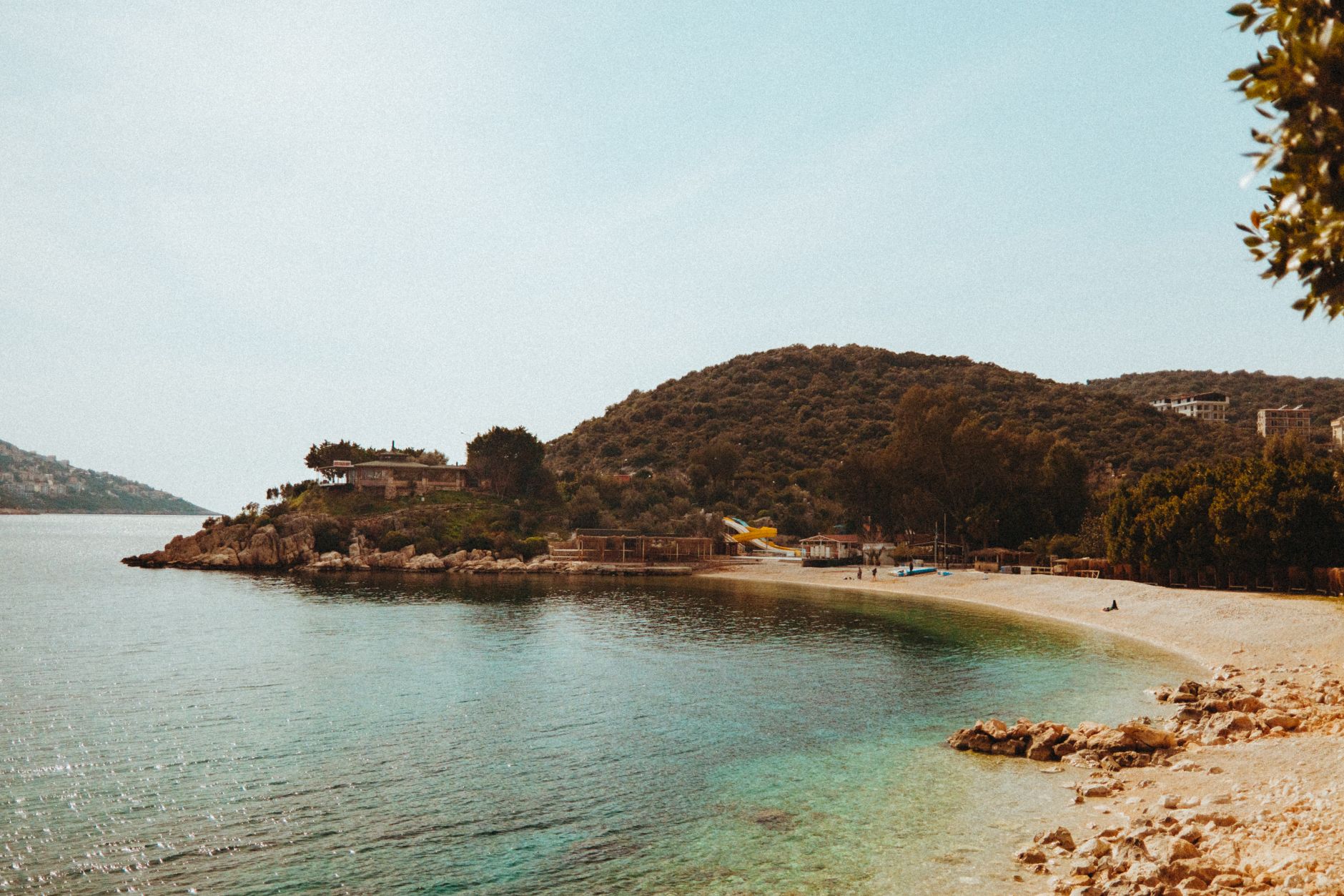 Relaxing beach scene with clear waters and lush greenery under a sunny sky, perfect for travel inspiration.