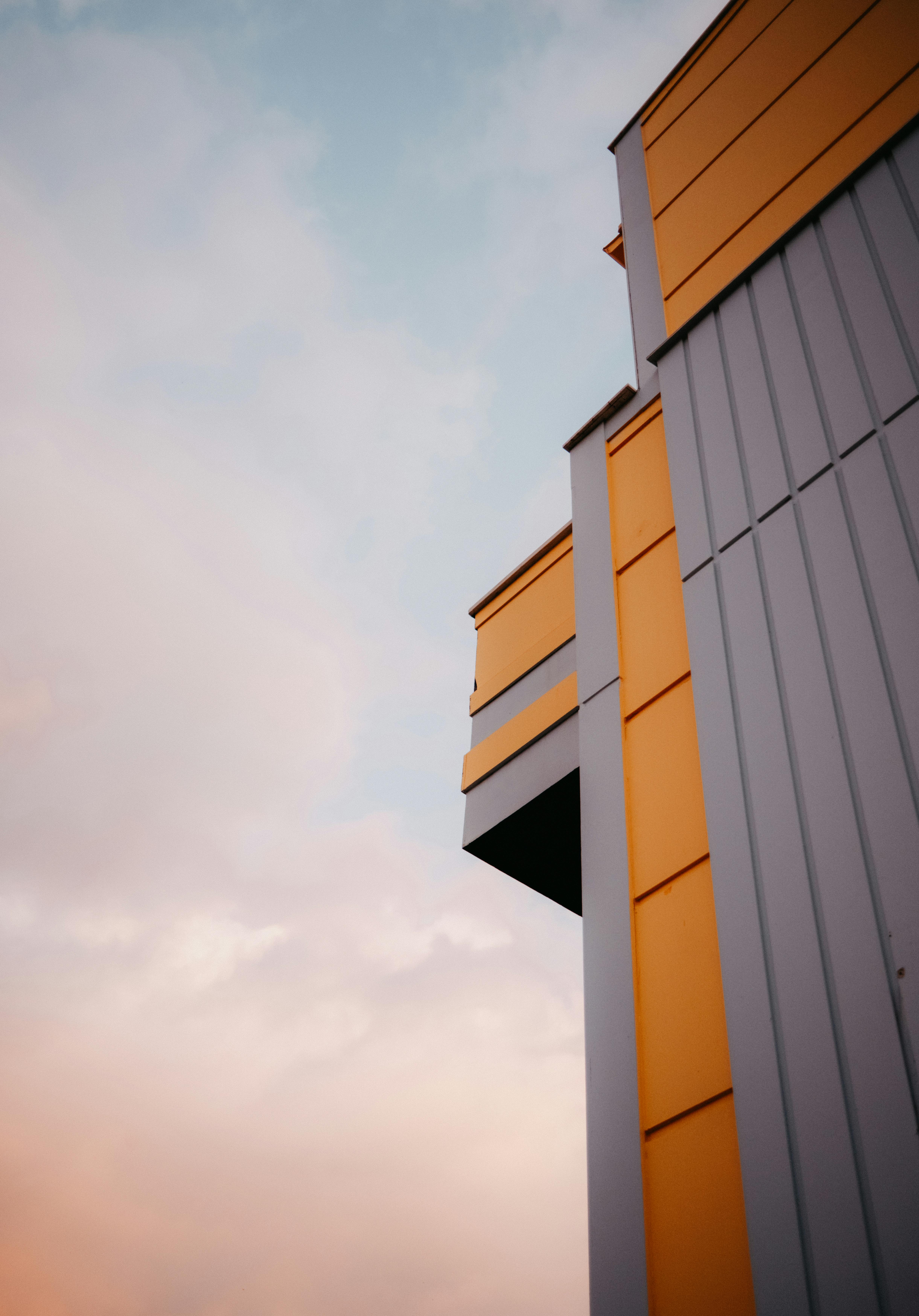 Gratis En moderne bygnings gule og grå facade står i kontrast til en pastelfarvet himmel. Lagerfoto