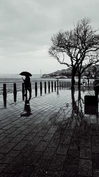 Monochrome scene of a person walking with an umbrella along İstanbul's rainy waterfront.