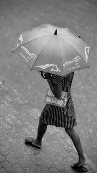 Black and white photo of a woman with an umbrella walking on a wet street