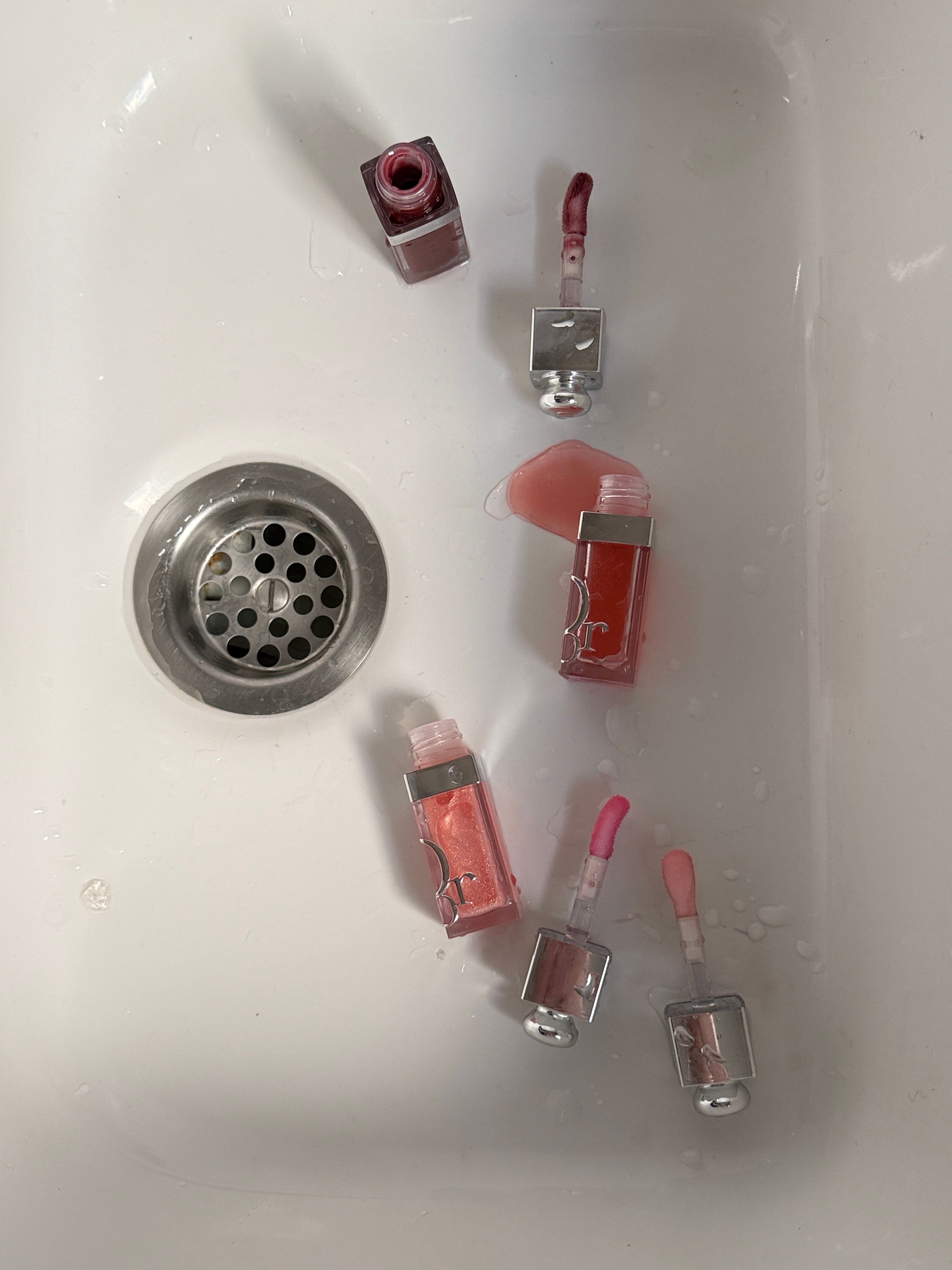 Assorted lip gloss tubes in a white sink creating a modern art composition.