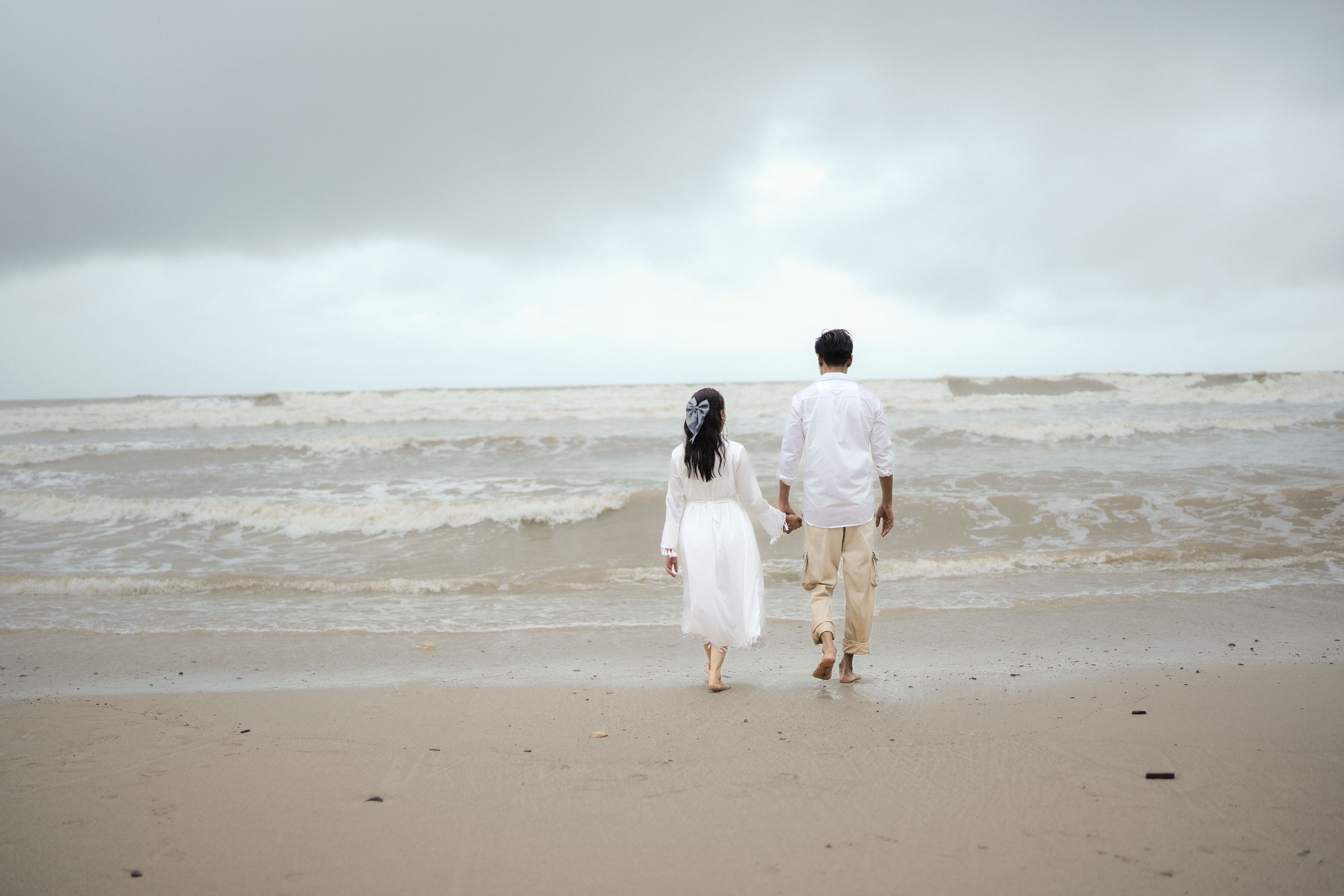 A romantic couple holding hands walking on Alibag Beach, Maharashtra, India.