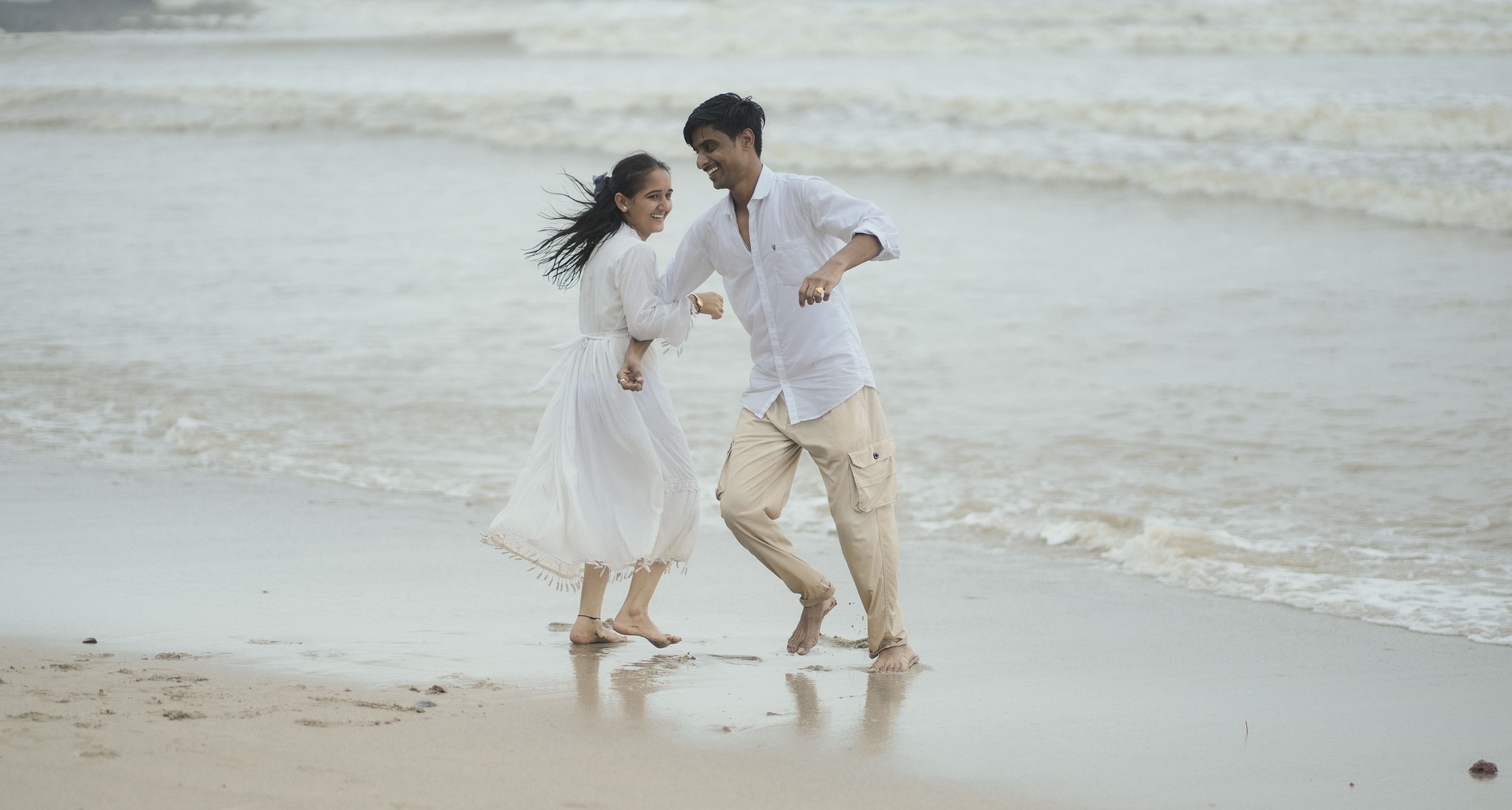 A joyful couple runs along the beach in Alibag, Maharashtra, India.