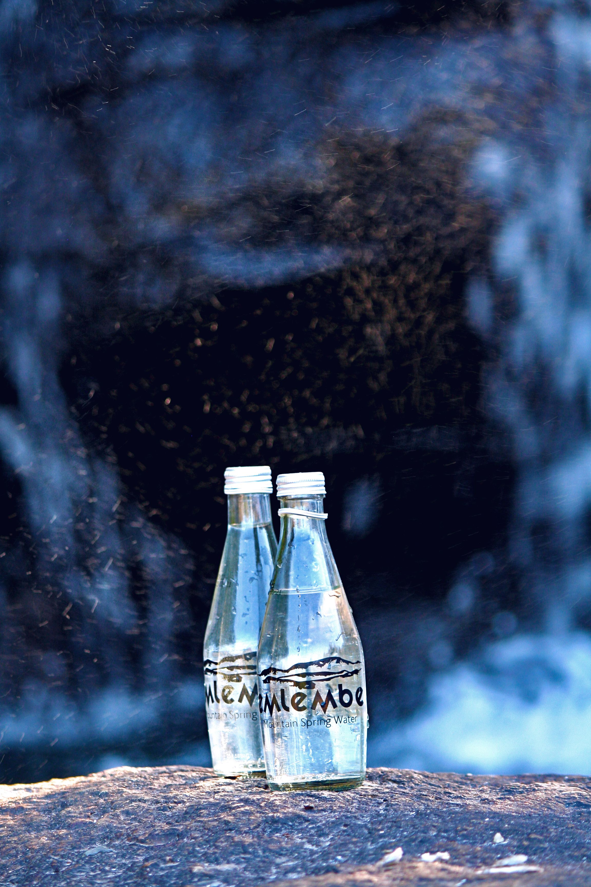 Two clear water bottles placed on a rock with a waterfall backdrop in Eswatini, capturing a moment of nature.