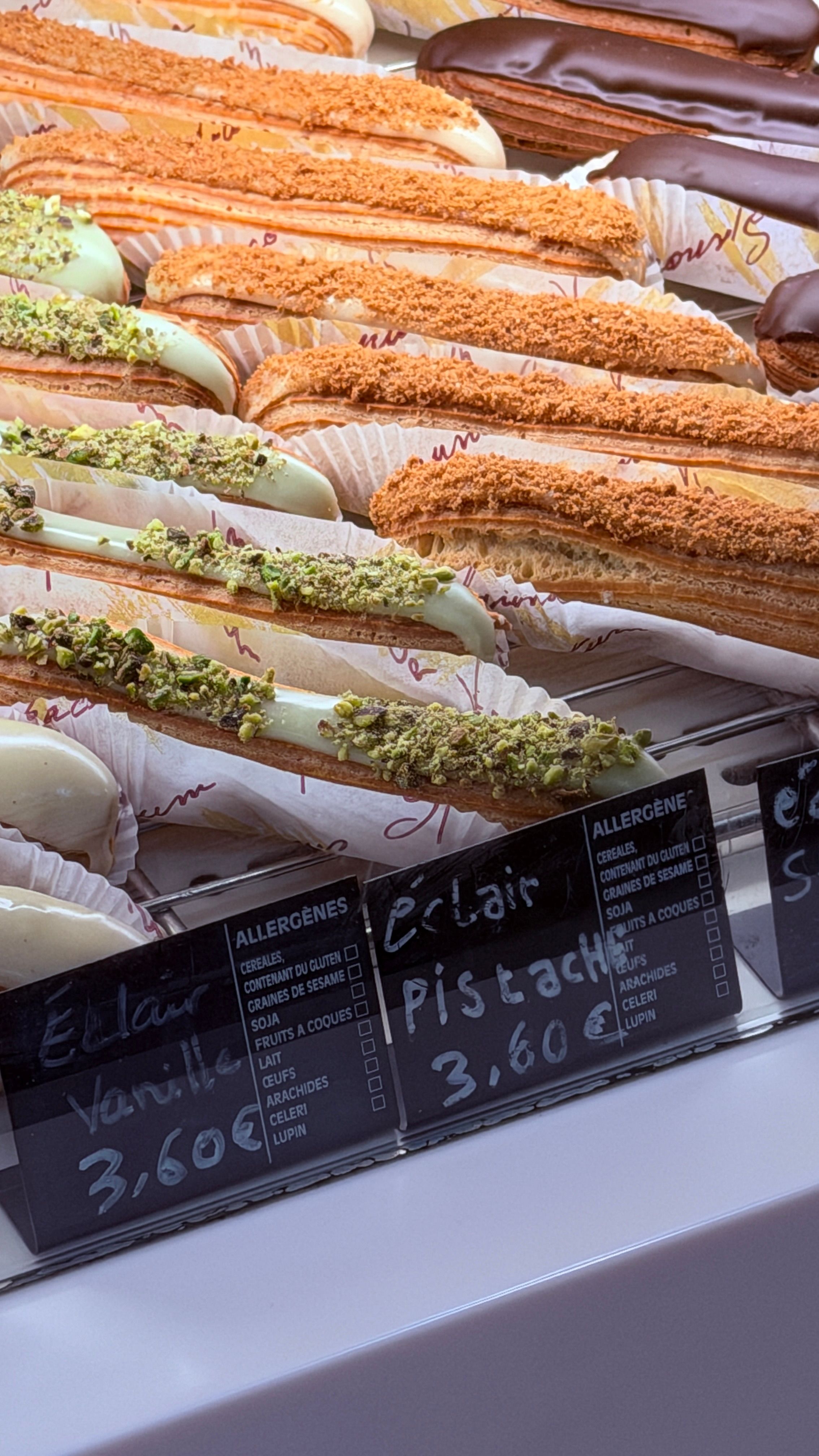 Parisian pastry display showcases assorted flavored eclairs topped with chocolate, pistachios, and more.
