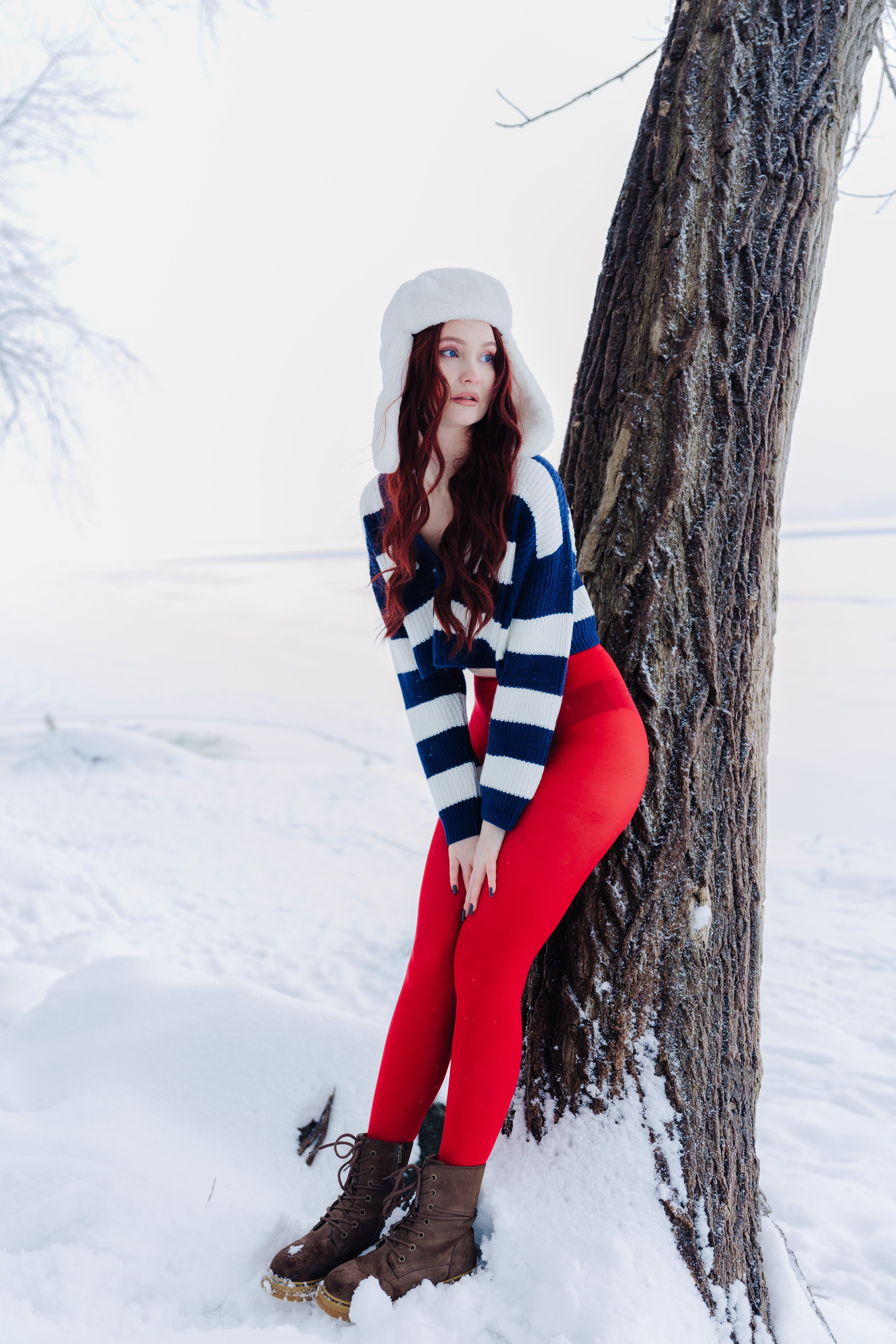 Woman in winter clothing posing by snow-covered tree outdoors