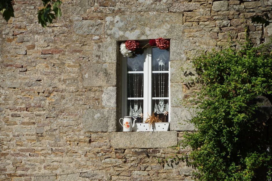 Rustic stone house window adorned with cotton curtains and plants.