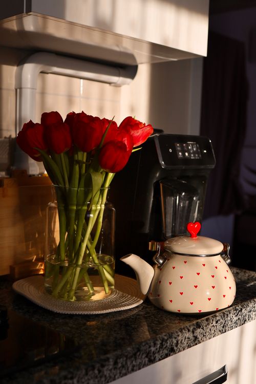 Free Warm kitchen scene with red tulips and heart-patterned teapot on a countertop. Stock Photo