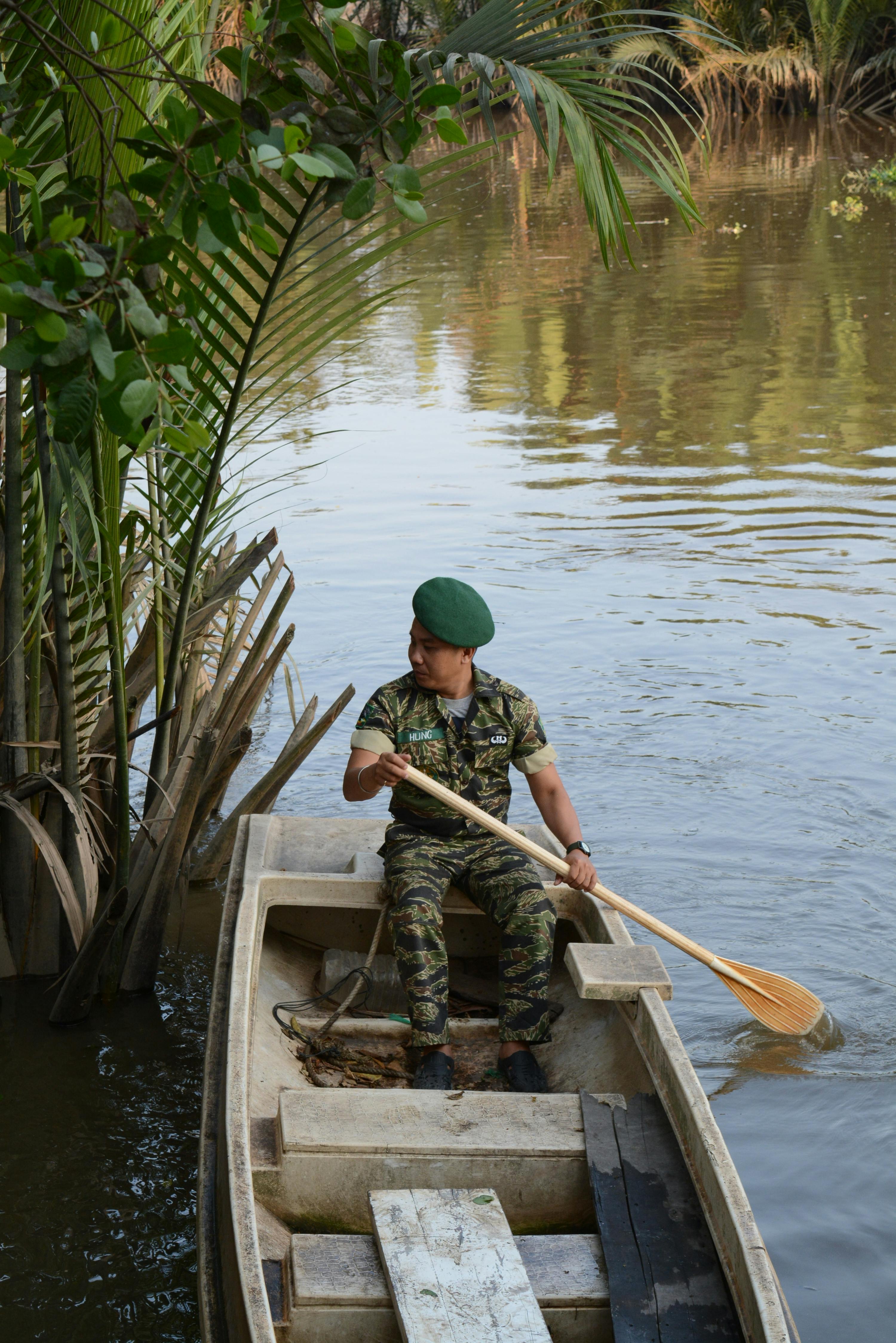 A soldier in camouflage paddles a boat through a jungle river, showcasing adventure and skill.