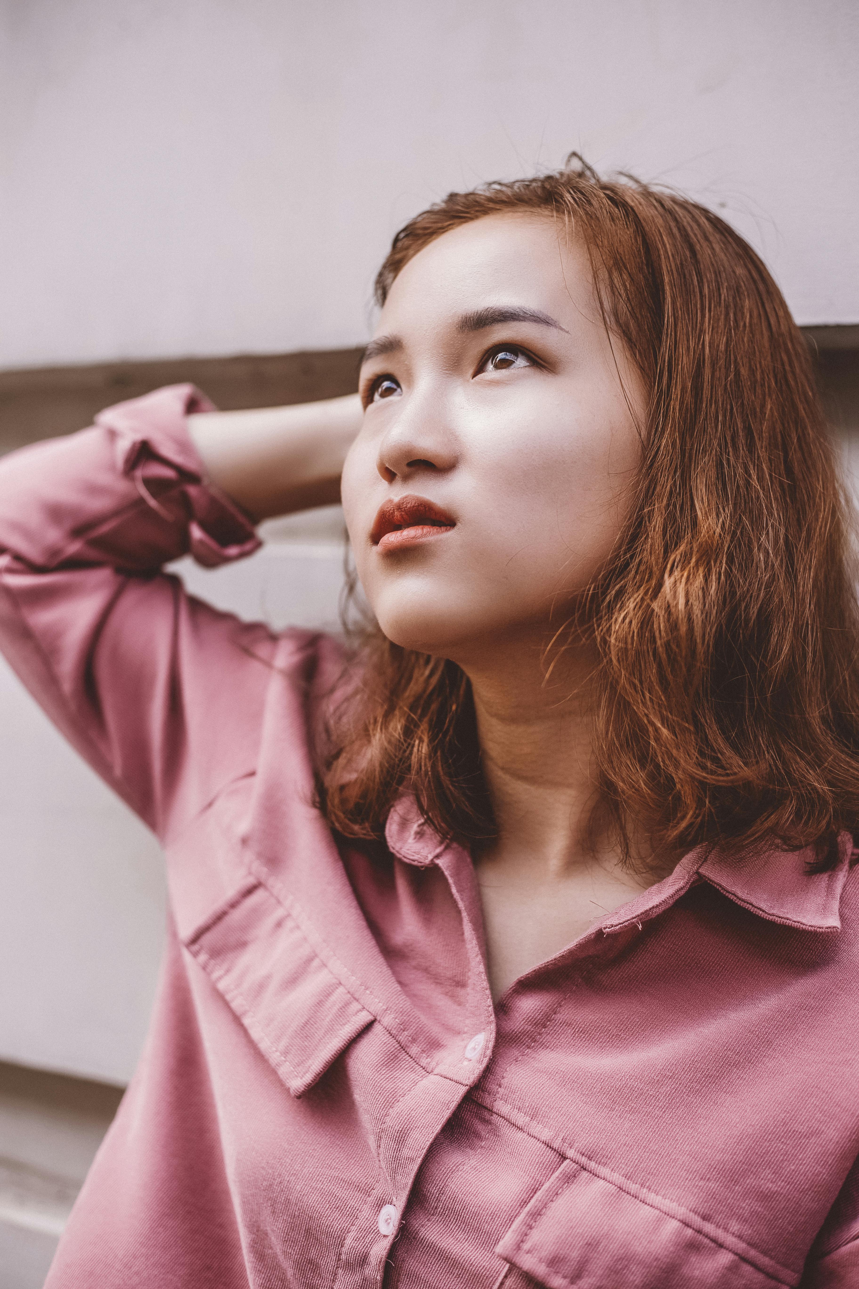 一名年轻女子身着粉色衬衫，若有所思地望向前方