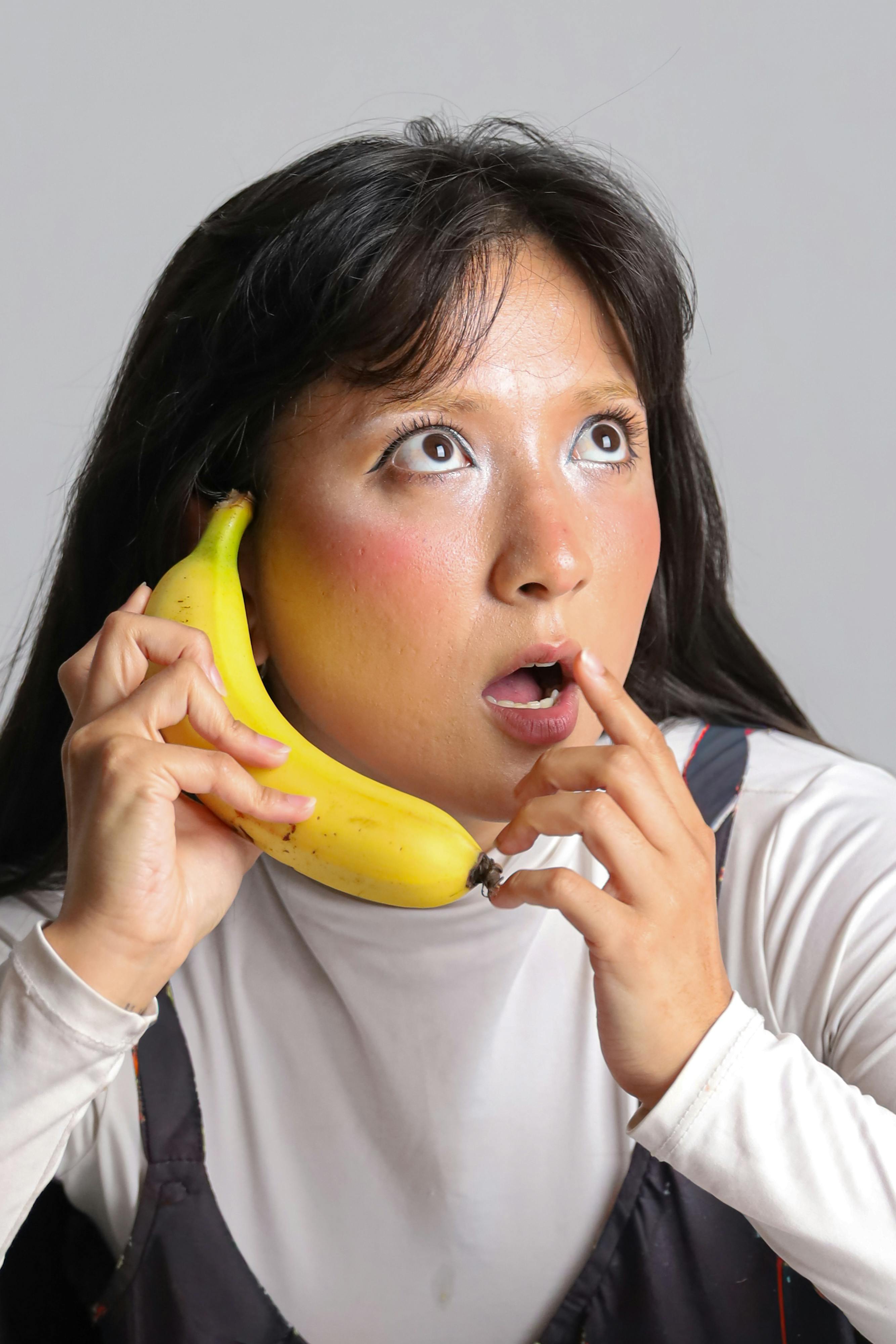 bezplatná Žena vtipně používá banán jako telefon a uvnitř ukazuje překvapený výraz. Základová fotografie