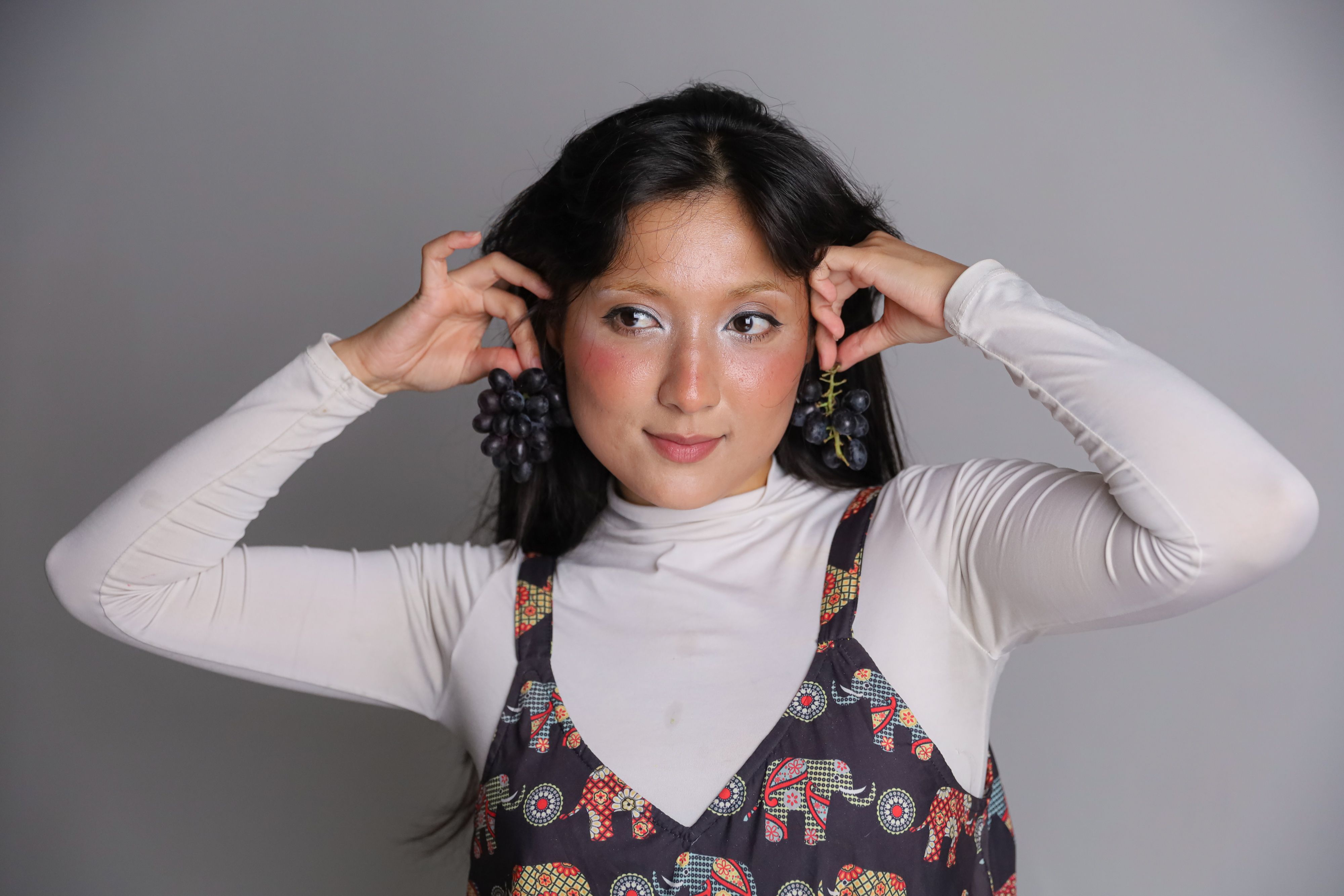 Portrait of a woman in a patterned dress and grape earrings, exuding creativity and fashion.