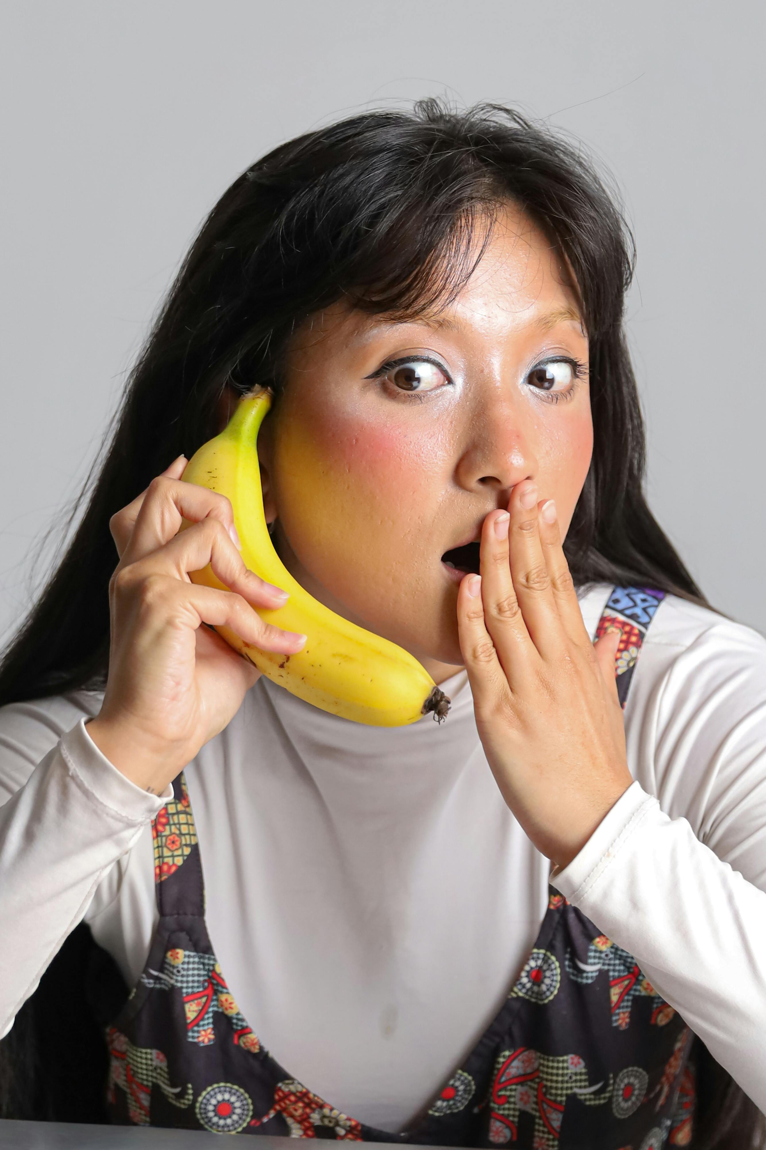 Kostnadsfria Lekfullt porträtt av en överraskad kvinna som låtsas att en banan är en telefon, vilket visar upp kreativitet och humor. Stock foto