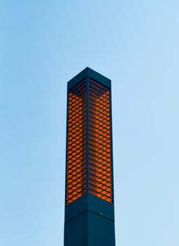A contemporary street lamp with an orange glow against a clear blue sky, showcasing minimalistic design.