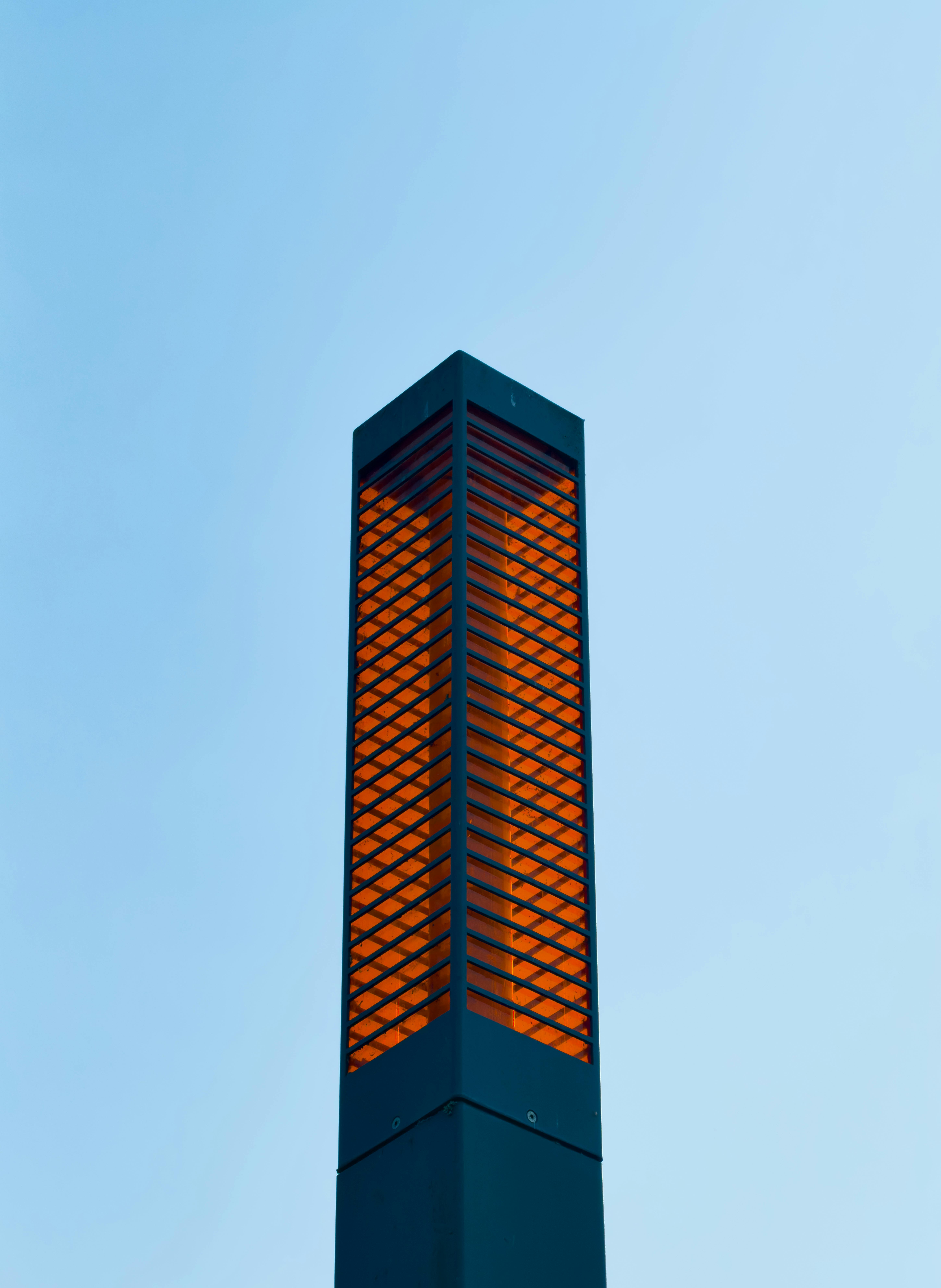 Free A contemporary street lamp with an orange glow against a clear blue sky, showcasing minimalistic design. Stock Photo