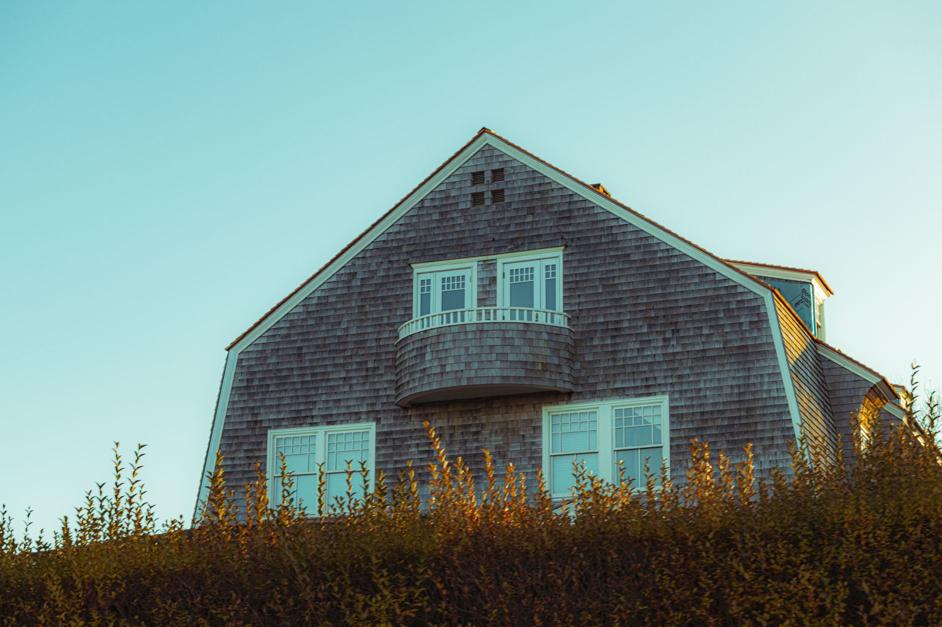 Cedar-shingled house with an elegant balcony, reflecting New England charm against a clear sky.