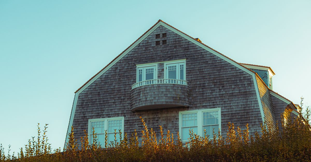 Cedar-shingled house with an elegant balcony, reflecting New England charm against a clear sky.