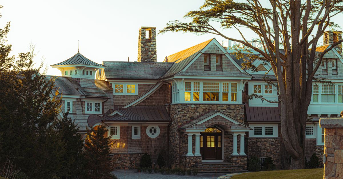 Elegant New England mansion with stone facade in a serene outdoor setting at sunset.