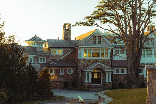 Elegant New England mansion with stone facade in a serene outdoor setting at sunset.