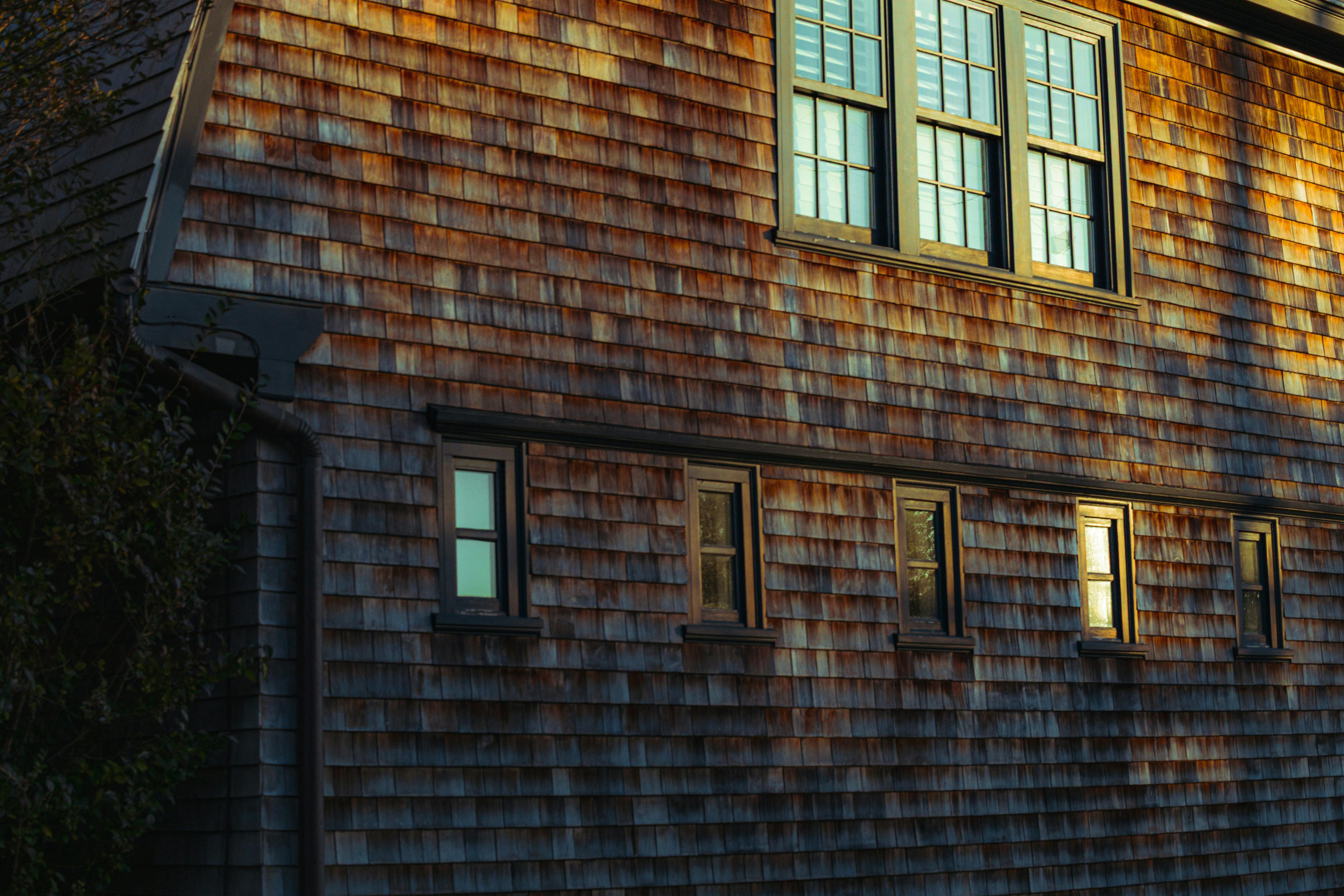 Sunlit cedar shingle facade of a coastal house with multiple windows, capturing the warmth of evening light.